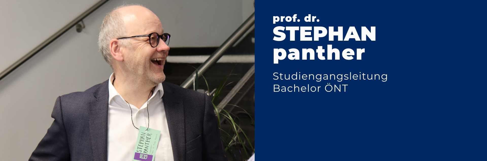 Professor Doktor Stephan Panther ist Studiengangsleiter des Bachelors Ökonomie - Nachhaltigkeit - Transformation. Auf dem Foto trägt er ein weißes Hemd, ein graues Sakko, eine Brille und lacht herzlich. 