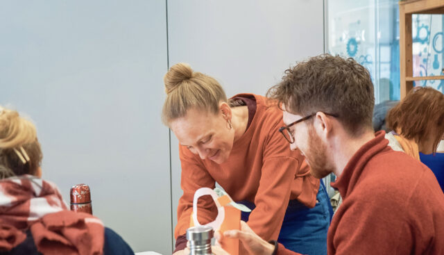 Lisanne Rother, Referentin für Impact- und Wissenschaftskommunikation an der Hochschule für Gesellschaftsgestaltung, liest gemeinsam mit einem Studierenden einen Text von einem Blatt, das auf einem Schreibtisch liegt.