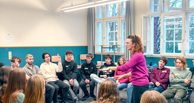 Kathrin-Twiesselmann-Steigerwald gibt einen 4FutureLab Workshop in einer Schulklasse. Sie steht hierbei mittig in einem Stuhlkreis und leitet Übungen an.