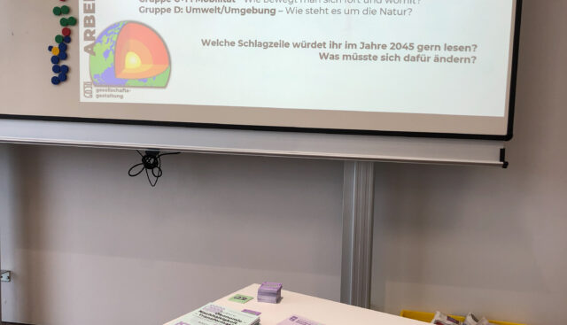 Mit einem Beamer wird eine Aufgabe zu einer Casual Layered Analysis (CLA) angestrahlt. Als Ergebnis der Aufgabe soll eine Schlagzeile stehen, die die Teilnehmenden 2045 gerne lesen würden. Zudem soll erörtert werden, was sich hierfür ändern müsste.