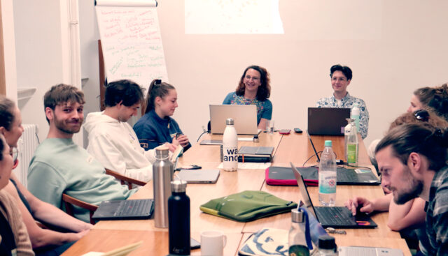 Die wissenschaftlichen Mitarbeitenden Kathrin Twiesselmann-Steigerwald und Paul Kühn der Hochschule für Gesellschaft sitzen frontal an einem Tisch vor acht interessierten Studierenden und halten ein 4FutureLab.